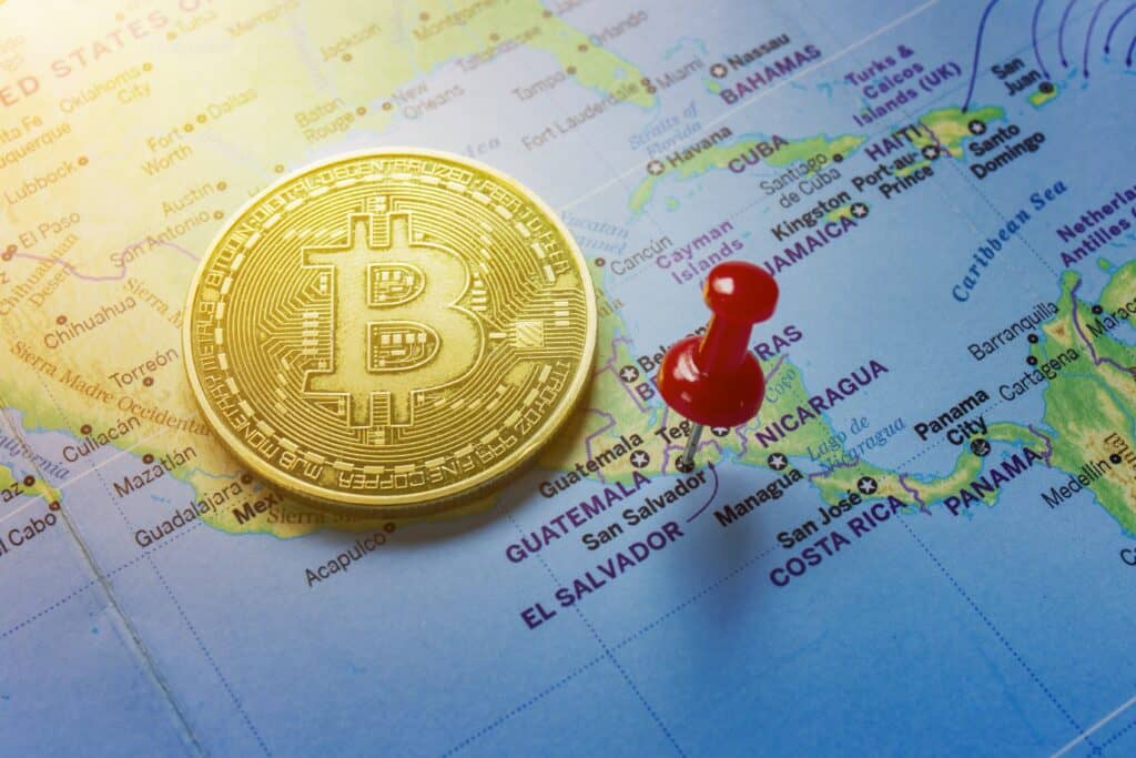 A red pin is pinned on the world map of El Salvador and there is a bitcoin next to it.