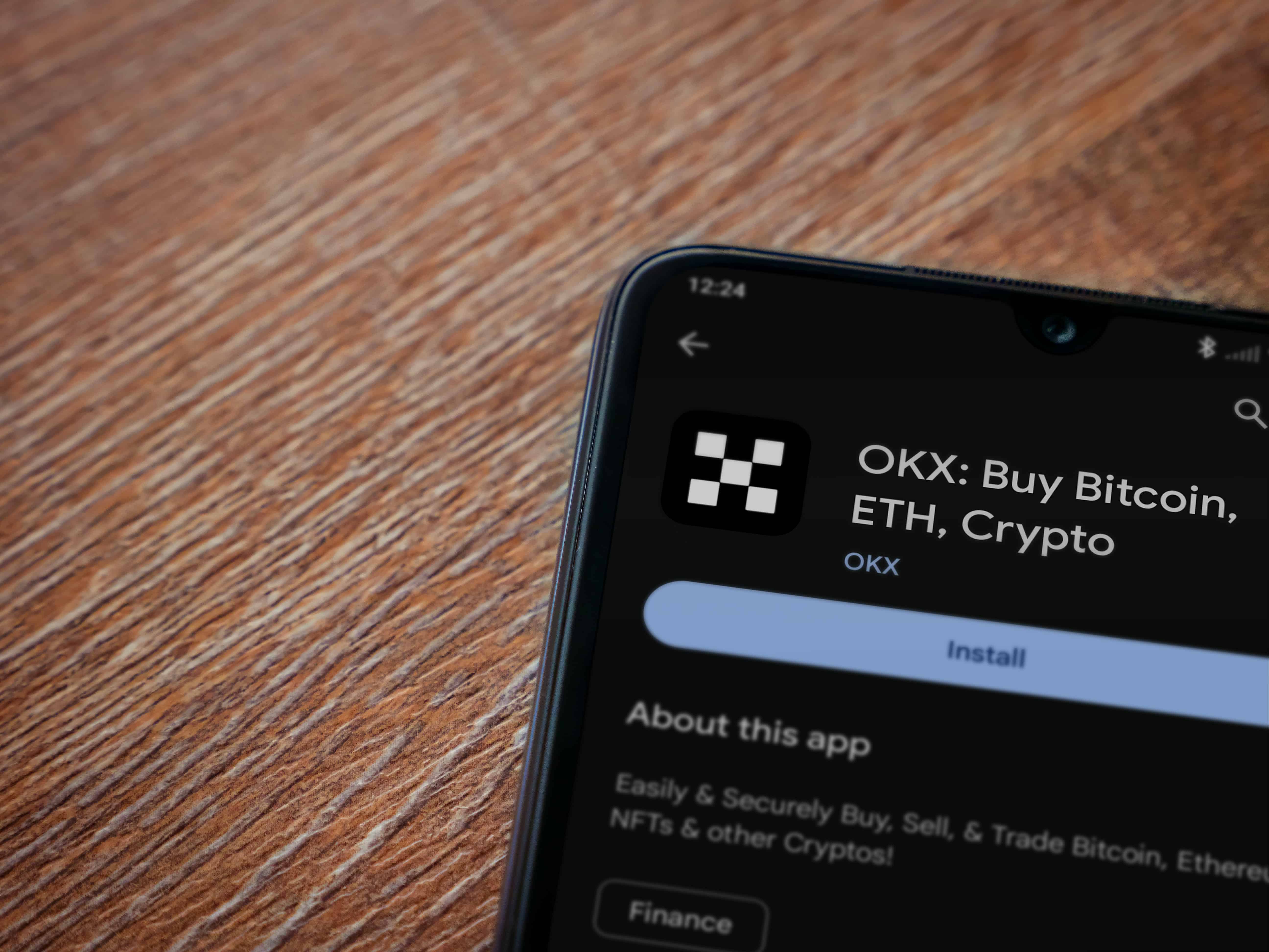 OKX app play store page on smartphone on wooden background.