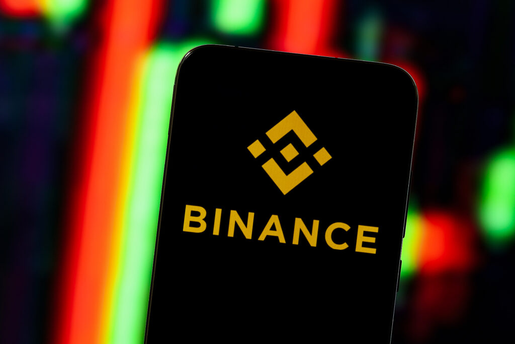 Binance logo displayed on a smartphone with candle sticks in the background