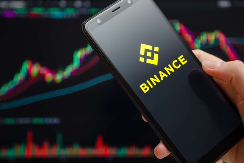 Binance mobile app running at smartphone screen with trading candlestick chart at background.