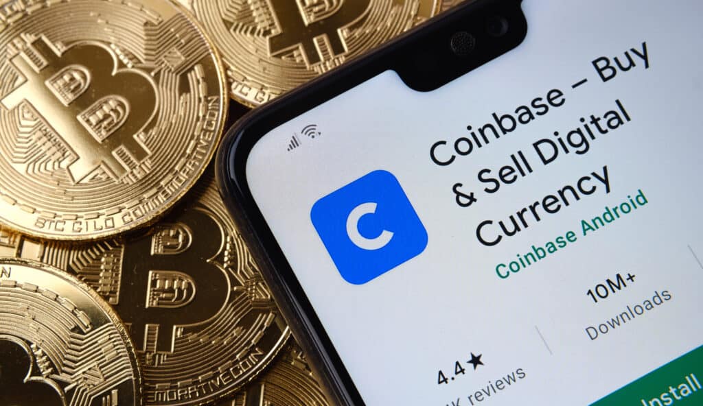 Coinbase app seen on the smartphone screen placed on top bitcoin coins pile.