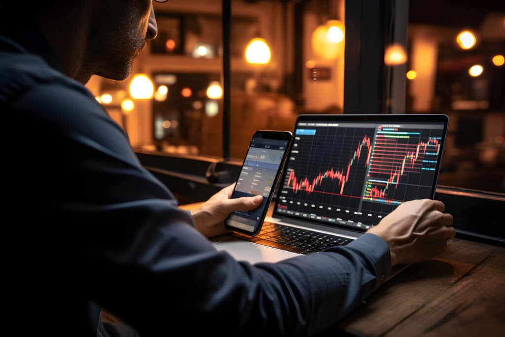 Investor using mobile phone and laptop checking trade market data.