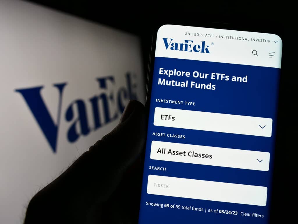 Person holding cellphone with webpage of US investment management company VanEck on screen in front of logo.