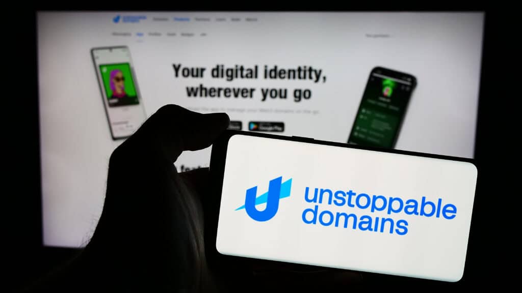 Person holding mobile phone with logo of American blockchain company Unstoppable Domains Inc. in front of web page.