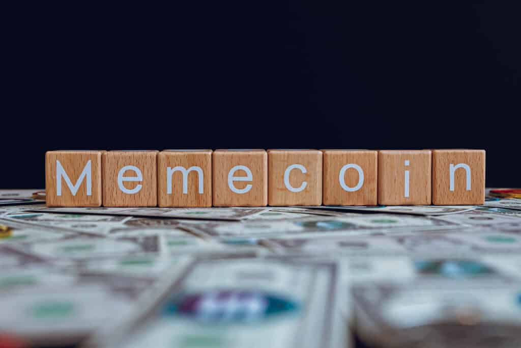 Wooden blocks with the text Memecoin on a black background and crypto banknotes scattered on the ground.