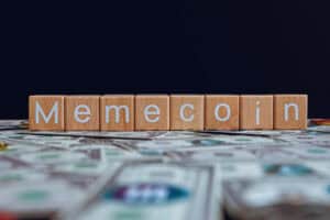 Wooden blocks with the text Memecoin on a black background and crypto banknotes scattered on the ground.