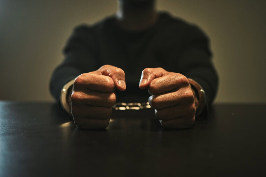 Interrogation, jail and hands of criminal in handcuffs for interview, investigation and arrested in station.