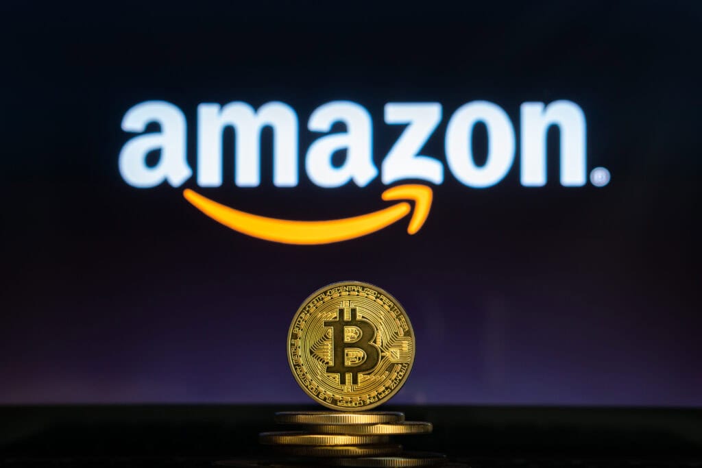 Bitcoin on a stack of coins with Amazon logo on a laptop screen.